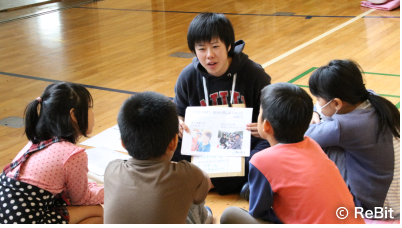 資料を読んでる職員を囲んだ子どもたちの写真